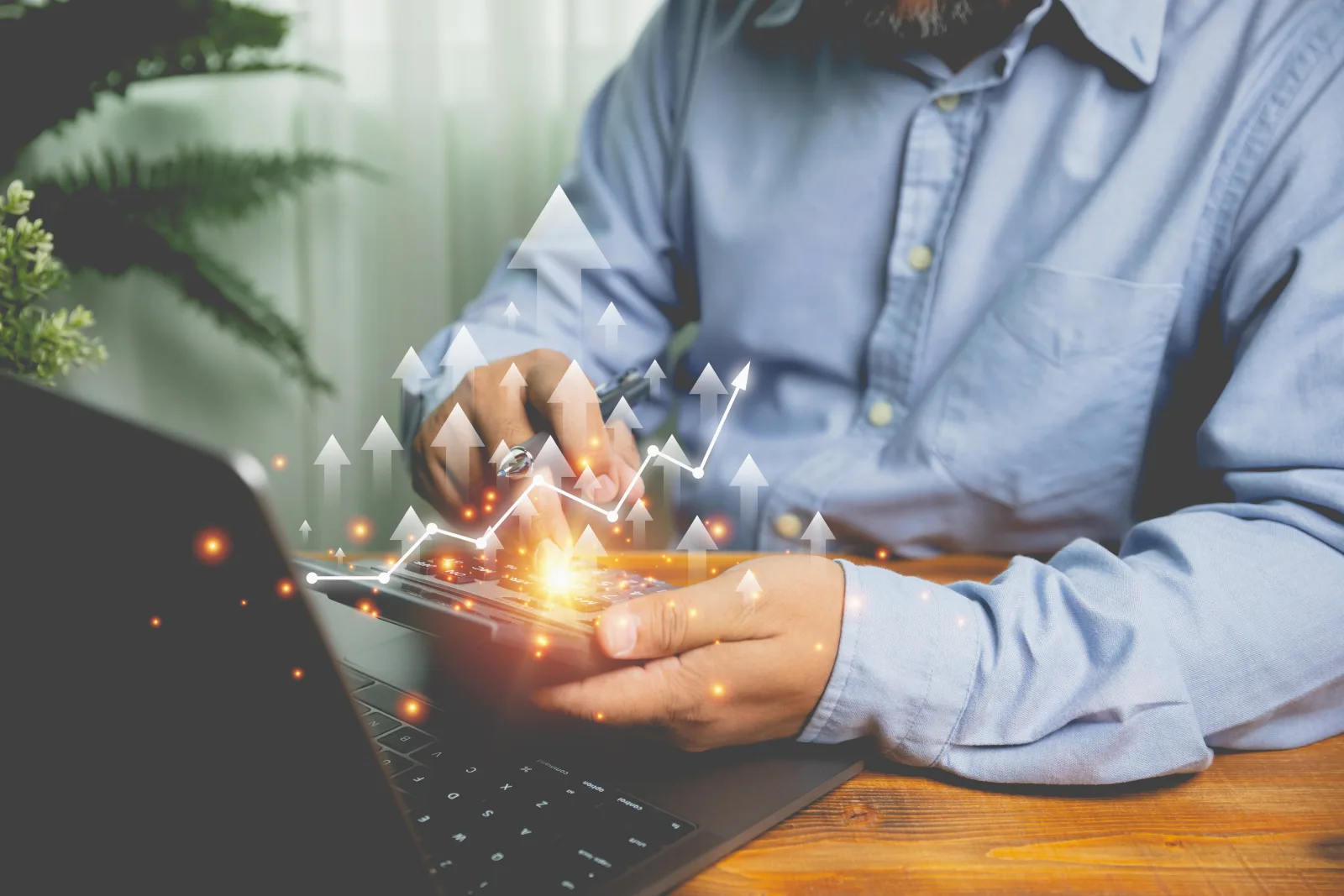 Un homme en chemise bleue utilise une calculatrice devant un ordinateur portable avec des graphiques de croissance