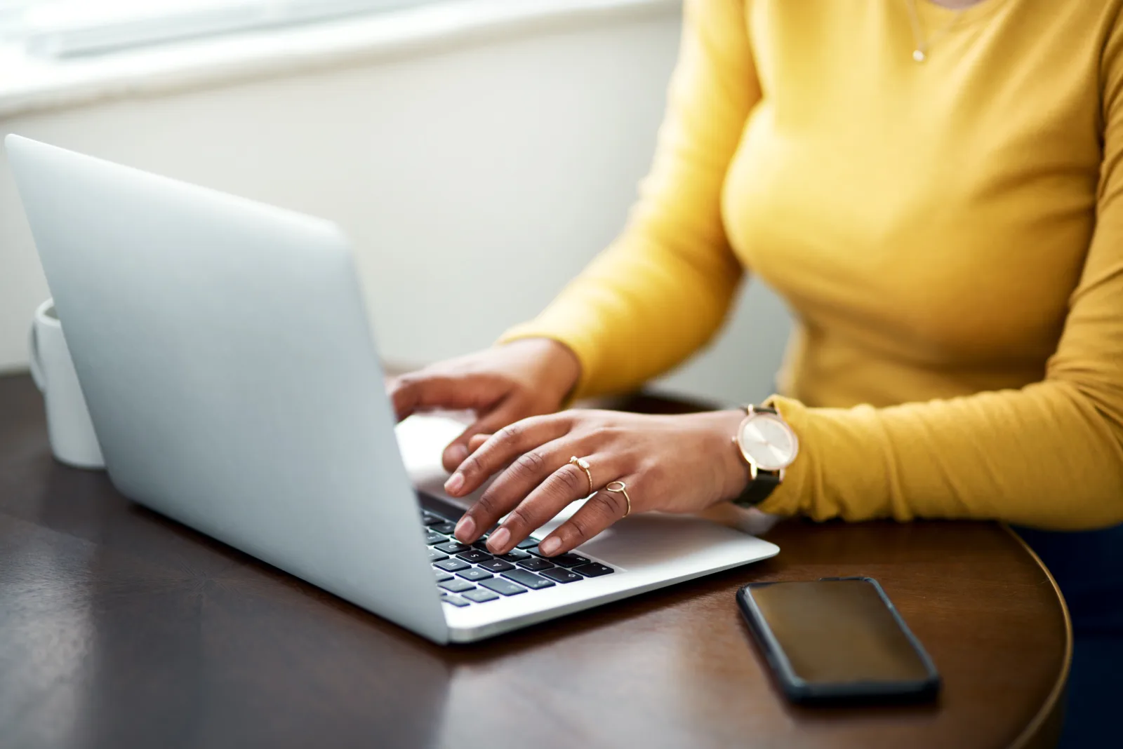 Une femme en haut jaune tape sur le clavier d'un ordinateur portable posé sur une table en bois